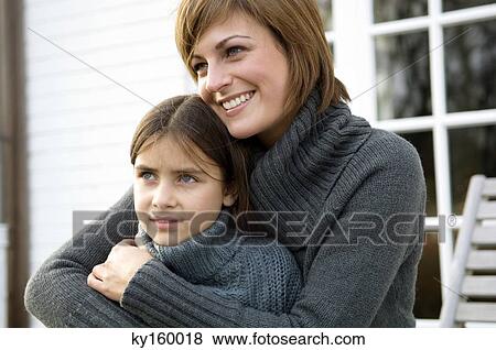 Close-up of a young woman hugging her daughter and smiling View Large Photo Image Stock Photo - Close-up of a young woman hugging her daughter and smiling. Fotosearch
