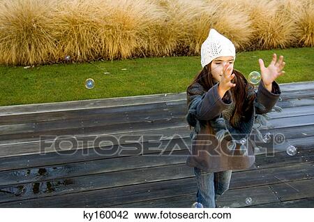 Girl standing on a boardwalk and catching bubbles View Large Photo Image Stock Image - Girl standing on a boardwalk and catching bubbles. Fotosearch