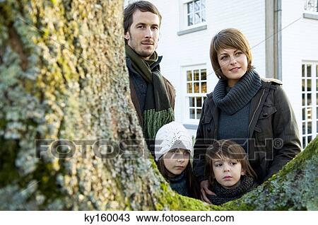 Stock Image - Two children standing near a tree with their parents. Fotosearch
