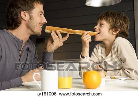 Mid adult man eating a baguette with his son View Large Photo Image Stock Photograph - Mid adult man eating a baguette with his son. Fotosearch