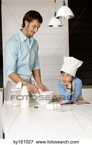 Mid adult man making a cake and his son in the kitchen View Large Photo Image Stock Photo - Mid adult man making a cake and his son in the kitchen. Fotosearch