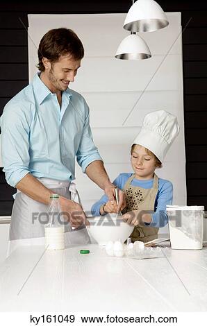 Mid adult man making a cake with his son in the kitchen View Large Photo Image Stock Photo - Mid adult man making a cake with his son in the kitchen. Fotosearch