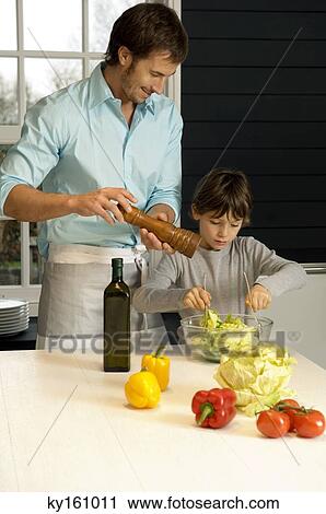Mid adult man preparing food with his son in the kitchen View Large Photo Image Stock Image - Mid adult man preparing food with his son in the kitchen. Fotosearch