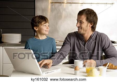 Stock Image - Mid adult man using a laptop and looking at his son. Fotosearch