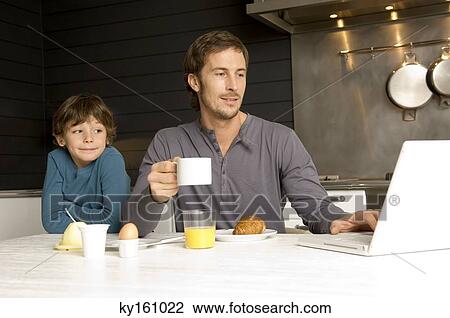 Mid adult man working on a laptop with his son standing behind him View Large Photo Image Stock Image - Mid adult man working on a laptop with his son standing behind him. Fotosearch