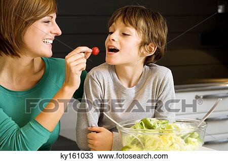 Young woman feeding a radish to her son View Large Photo Image Stock Image - Young woman feeding a radish to her son. Fotosearch