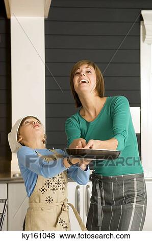 Young woman holding a frying pan with her son and smiling View Large Photo Image Stock Photo - Young woman holding a frying pan with her son and smiling. Fotosearch