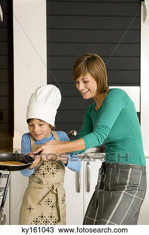 Stock Image - Young woman preparing a pancake with her son. Fotosearch