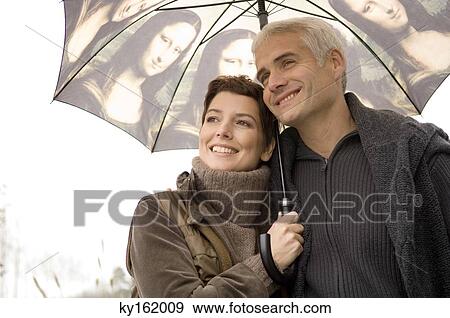 Stock Photo - Close-up of a mid adult woman and a mature man under an umbrella. Fotosearch