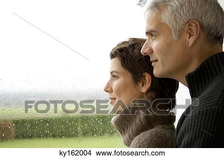 Mature man and a mid adult woman looking out through a window View Large Photo Image Picture - Mature man and a mid adult woman looking out through a window. Fotosearch