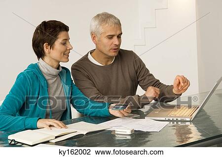 Mature man and a mid adult woman working on a laptop and holding a credit card View Large Photo Image Stock Image - Mature man and a mid adult woman working on a laptop and holding a credit card. Fotosearch