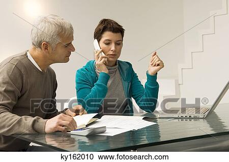 Mature man calculating bills and a mid adult woman talking on a mobile phone beside him View Large Photo Image Stock Image - Mature man calculating bills and a mid adult woman talking on a mobile phone beside him. Fotosearch
