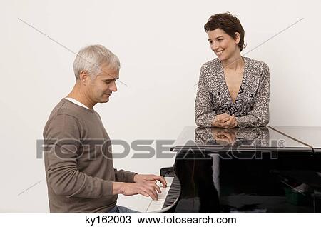 Mature man playing a piano and a mid adult woman standing near him View Large Photo Image Stock Image - Mature man playing a piano and a mid adult woman standing near him. Fotosearch