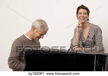 Mature man playing a piano and a mid adult woman standing near him View Large Photo Image Stock Image - Mature man playing a piano and a mid adult woman standing near him. Fotosearch