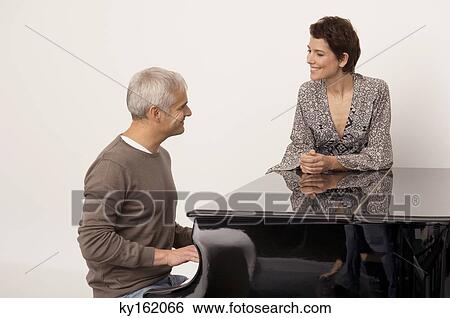 Mature man playing a piano and a mid adult woman standing near him View Large Photo Image Stock Photograph - Mature man playing a piano and a mid adult woman standing near him. Fotosearch