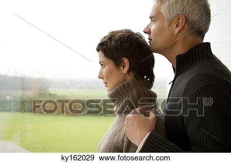 Mid adult woman and a mature man looking out through a window View Large Photo Image Stock Photo - Mid adult woman and a mature man looking out through a window. Fotosearch