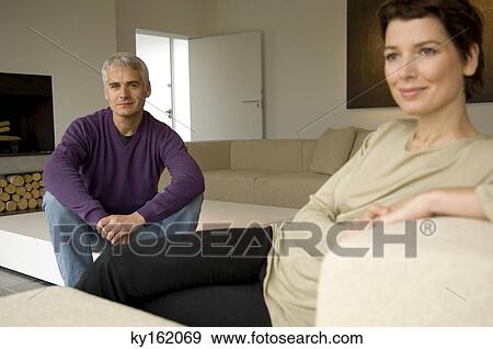 Mid adult woman and a mature man sitting in a living room View Large Photo Image Stock Photo - Mid adult woman and a mature man sitting in a living room. Fotosearch