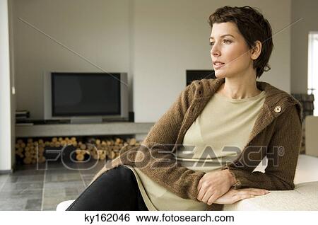 Mid adult woman leaning against a couch View Large Photo Image Stock Photograph - Mid adult woman leaning against a couch. Fotosearch
