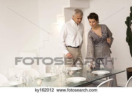 Mid adult woman setting a dining table and a mature man standing beside her View Large Photo Image Stock Image - Mid adult woman setting a dining table and a mature man standing beside her. Fotosearch
