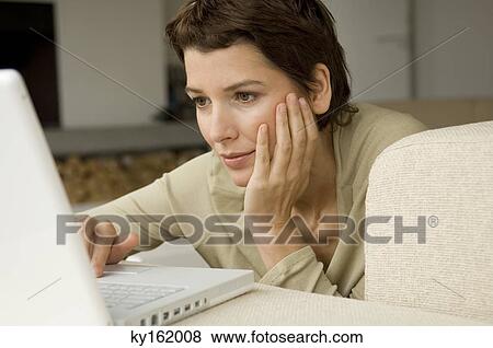 Mid adult woman working on a laptop in a living room View Large Photo Image Stock Photo - Mid adult woman working on a laptop in a living room. Fotosearch