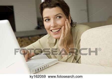 Mid adult woman working on a laptop in a living room View Large Photo Image Stock Photo - Mid adult woman working on a laptop in a living room. Fotosearch