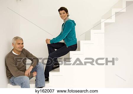 Stock Photo - Portrait of a mature man and a mid adult woman sitting on a staircase. Fotosearch