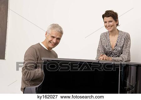 Portrait of a mature man playing a piano and a mid adult woman standing near him View Large Photo Image Stock Photo - Portrait of a mature man playing a piano and a mid adult woman standing near him. Fotosearch