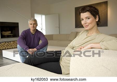 Stock Image - Portrait of a mid adult woman and a mature man sitting in a living room. Fotosearch
