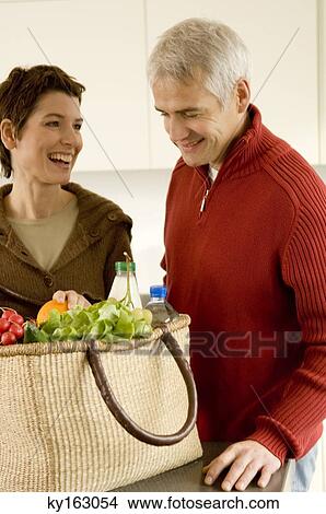 Picture - Mature man and a mid adult woman standing in the kitchen. Fotosearch