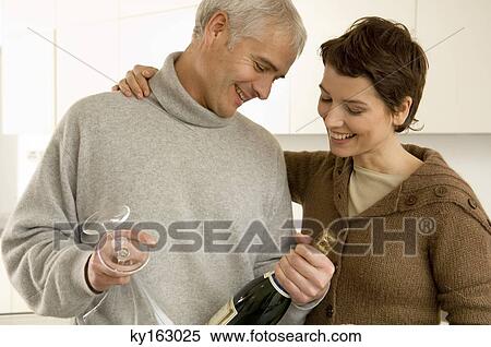 Mature man and a mid adult woman looking at a champagne bottle View Large Photo Image Stock Photography - Mature man and a mid adult woman looking at a champagne bottle. Fotosearch