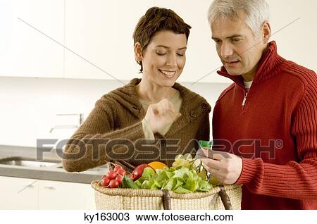 Stock Image - Mature man holding a bunch of grapes with a mid adult woman standing beside him. Fotosearch