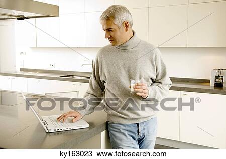 Stock Image - Mature man working on a laptop in the kitchen. Fotosearch