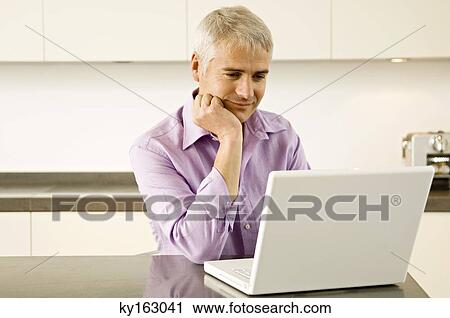 Mature man working on a laptop in the kitchen View Large Photo Image Stock Image - Mature man working on a laptop in the kitchen. Fotosearch