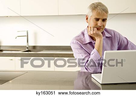 Mature man working on a laptop in the kitchen View Large Photo Image Stock Image - Mature man working on a laptop in the kitchen. Fotosearch