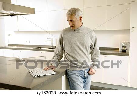 Mature man working on a laptop in the kitchen View Large Photo Image Stock Photo - Mature man working on a laptop in the kitchen. Fotosearch