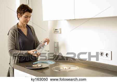Mid adult woman holding a bottle in the kitchen View Large Photo Image Stock Image - Mid adult woman holding a bottle in the kitchen. Fotosearch