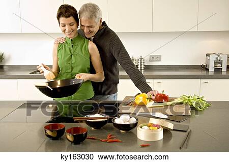Mid adult woman preparing food with a mature man standing with arm around her in the kitchen View Large Photo Image Stock Image - Mid adult woman preparing food with a mature man standing with arm around her in the kitchen. Fotosearch