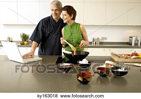 Mid adult woman preparing food with a mature man using a laptop in the kitchen View Large Photo Image Stock Photo - Mid adult woman preparing food with a mature man using a laptop in the kitchen. Fotosearch