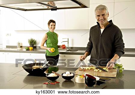 Stock Image - Portrait of a mature man and a mid adult woman preparing food in the kitchen. Fotosearch