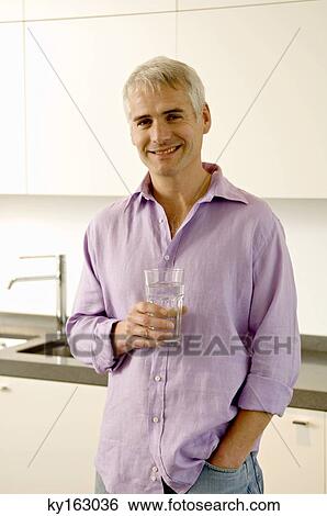 Portrait of a mature man holding a glass of water in the kitchen View Large Photo Image Stock Photograph - Portrait of a mature man holding a glass of water in the kitchen. Fotosearch