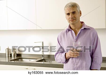 Portrait of a mature man holding a glass of water in the kitchen View Large Photo Image Stock Photography - Portrait of a mature man holding a glass of water in the kitchen. Fotosearch