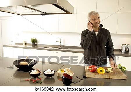 Stock Image - Portrait of a mature man talking on a mobile phone in the kitchen. Fotosearch