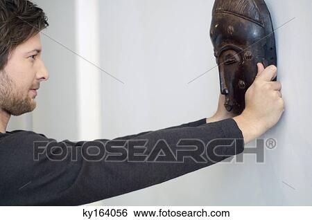 Mid adult man adjusting a mask on a wall View Large Photo Image Stock Photograph - Mid adult man adjusting a mask on a wall. Fotosearch