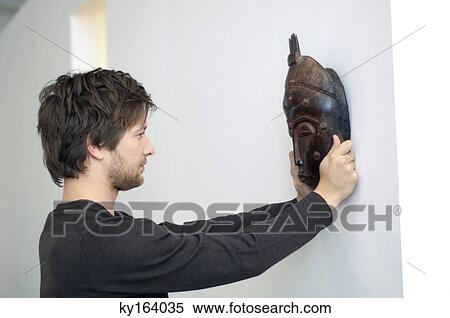 Mid adult man adjusting a mask on a wall View Large Photo Image Stock Photography - Mid adult man adjusting a mask on a wall. Fotosearch
