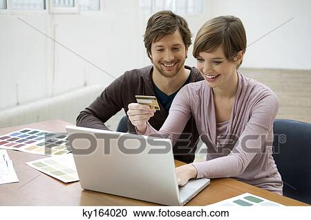 Mid adult man and a young woman using a laptop and holding a credit card View Large Photo Image Stock Image - Mid adult man and a young woman using a laptop and holding a credit card. Fotosearch