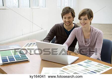 Stock Image - Mid adult man and a young woman using a laptop. Fotosearch