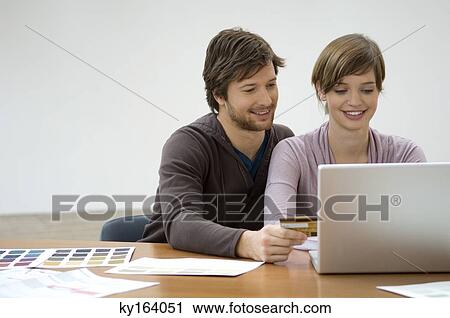Stock Image - Mid adult man and a young woman using a laptop and holding a credit card. Fotosearch