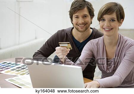 Mid adult man and a young woman using a laptop and holding a credit card View Large Photo Image Stock Photo - Mid adult man and a young woman using a laptop and holding a credit card. Fotosearch