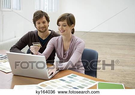 Mid adult man and a young woman using a laptop and holding a credit card View Large Photo Image Stock Photograph - Mid adult man and a young woman using a laptop and holding a credit card. Fotosearch