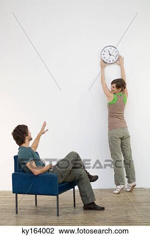 Mid adult man looking at his wife mounting a clock on the wall View Large Photo Image Stock Image - Mid adult man looking at his wife mounting a clock on the wall. Fotosearch